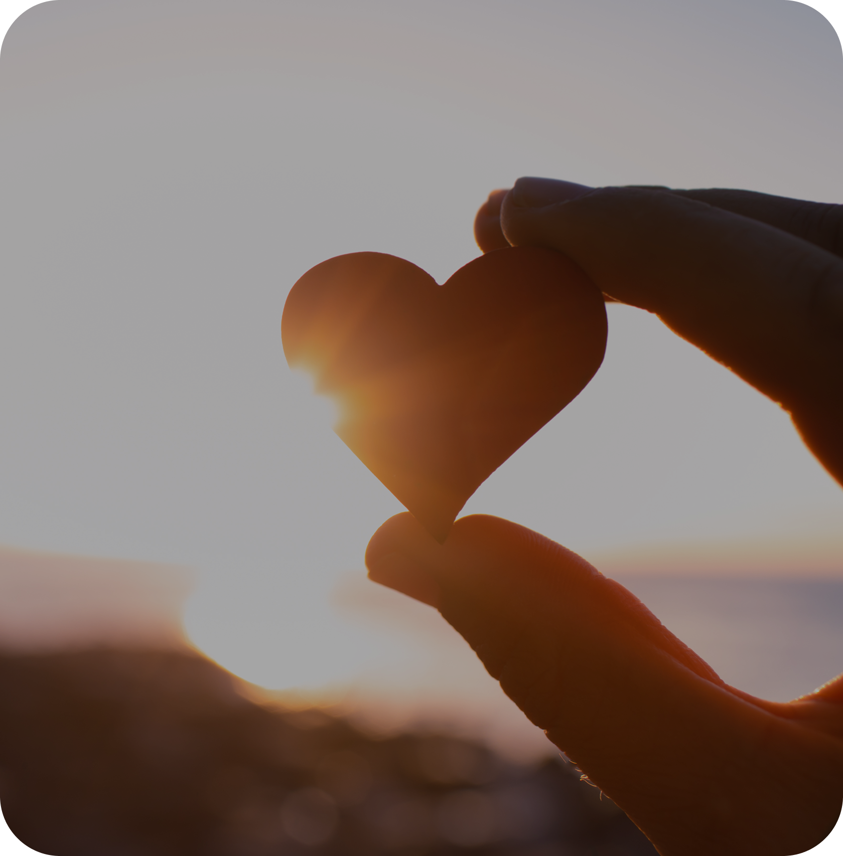 Hand holding heart shape at sunset